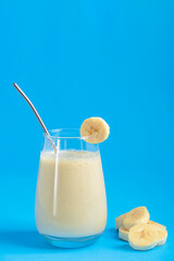 One glass of protein organic smoothie or milkshake made of ripe sweet banana fruit blended and mixed with milk served with zero waste metal straw on brigth blue background. Image with copy space