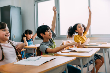 Elementary age Asian student boy raised hands up in class. Diverse group of pre-school pupils in...