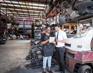 African saleswoman recommends automotive spare parts for a customer from a tablet computer in warehouse automotive parts.