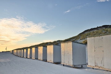 Horizontal view on a row of beach cabins at sunset in spring. North sea beach with dunes in Zeeland on a sunny day. Copy space.