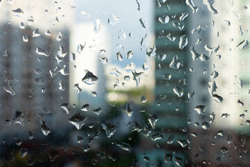 Window glass with rain drops on the background of a blurred cityscape
