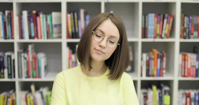 Young beautiful european female student wearing glasses smiling cheerfully posing for camera in college library. Closeup. Education concept.