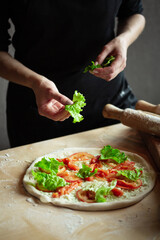 Hands of chef preparing pizza. Putting ingredients on rolled dough