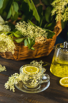 Herbal health tea of elder flower surrounded fresh flowers and leaves in basket, dark rustic style
