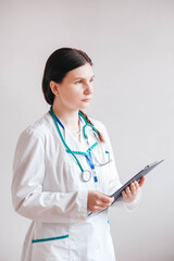 Friendly female doctor in a white coat with a folder in his hands and a stethoscope on a white background. Copy, empty space for text