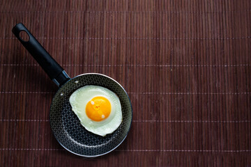 Frying pan with fried egg on a bamboo table