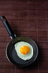 Frying pan with fried egg on a bamboo table