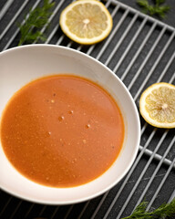 Bowl of orange curry soup. Spicy oriental dish. Pan-Asian cuisine. Top view of food plate at black grill grid on blurred background. Close up shot. Soft focus.