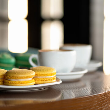 Macaroons yellow pastries and coffee. French dessert or almond sweets on wooden table. Blank or template for banner or greeting card. Copy space at top of image. Soft focus. 