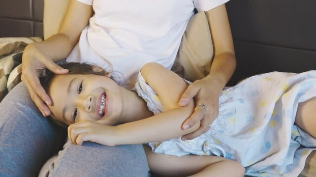Adorable 5 years' old asian girl is laying on mother's lap with smiling to listening bedtime story and spending good family relation moment which shows relax, enjoy, happy and positive togetherness.