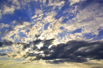 The bright sun hid behind light white clouds in the blue sky.