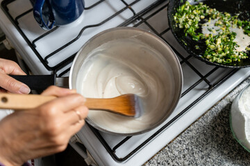Woman cooking bechamel sauce at home. Close up.