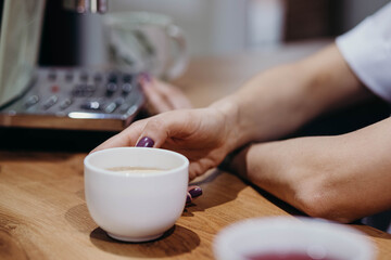 Waitress serving cappuccino to the customer. Female hands bring hot aromatic brewed coffee to the guest, close-up view