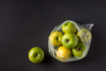 single use plastic packaging issue. green apples in plastic bags  on a dark background