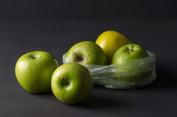 Transparent plastic crumpled cellophane bag with group of ripe green and yellow apples on a black background. Ecology concept