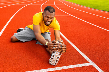 Young focused attractive African American athlete sportsman stretching on racetrack at city...