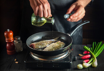 Professional chef prepares fresh fish in a pan with oil. Preparation for cooking fish food. Working environment in the kitchen of a restaurant or cafe