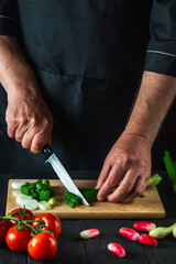 Chef is hands close-up cuts young green onions on a restaurant kitchen cutting board for salad. Vegetable diet or snack idea
