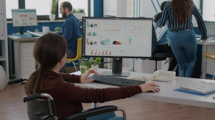Handicapped businesswoman analysing financial statistics sitting in wheelchair checking graphs from computer in start up business office. Disabled employee working with team using modern technology - Powered by Adobe
