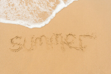 Word SUMMER handwritten on the sand of beach