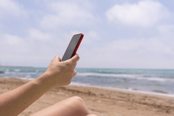 Unrecognizable woman using smart phone on the beach.Hand holding cellphone on summer holidays background.