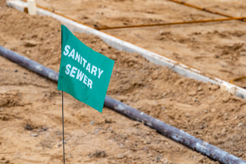Small green flag with white lettering, warning of an underground sanitary sewer line, at a new home construction site.