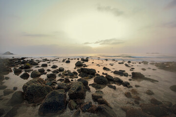 Sunrise at beach with lost of rocks and waves hitting on rocks and slow shutter speed on the water. Beach sunrise with fog