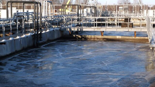 Huge pool of swirling aerating water with technical grounds at contemporary purification station at sunset in winter evening