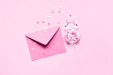 Pink alarm clock with decorative colored hearts and envelope on pink background. Festive concept or Romantic Love message. Monochrome. Creative copy space