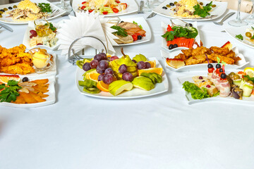 Salads appetizers and fruits on a buffet table with a white tablecloth.