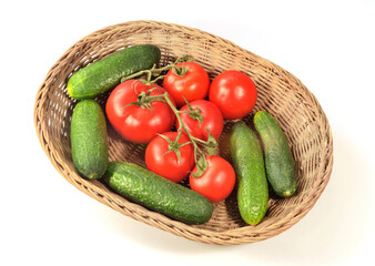 tomatoes and cucumbers lie in a wicker basket isolated on white background