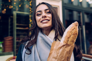 Smiling woman with baguette in paper bag near bakery
