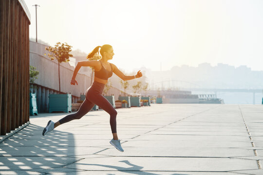Side view image of a brunette running on the pavement outdoors. Low angle