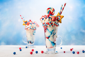 Crazy milk shake with ice cream,whipped cream, marshmallow,cookies and colored candy in glass. Sweet dessert for Fourth of July. Idea milkshake for Patriotic day. - obrazy, fototapety, plakaty