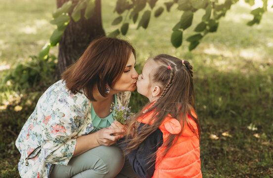 Young mother kisses her daughter in the park in the summer. concept of a happy family, the relationship of mother and child