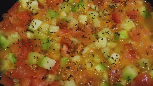 Boiling vegetables stewed in a frying pan - tomatoes and zucchini, sprinkled with dry cumin
