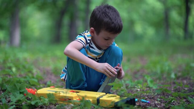 A boy loads a clip with cartridges from a toy machine gun outdoors