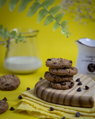 cookies empilhados em tabua de madeira com fundo amarelo com gotas de chocolate