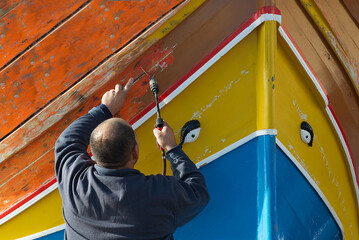 Rear view of a man stripping paint off a traditional luzzu boat with a blowtorch, Marsaxlokk, Malta