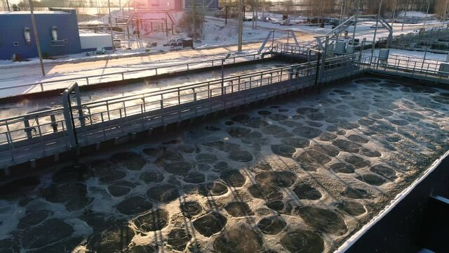 Large pool with swirling foamy aerating water and bridge at contemporary purification station in winter evening upper view