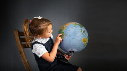 Girl child schoolgirl in school uniform with globe, classic school photos, dark background