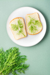 Sandwiches of white bread and fresh dill on a plate and a bunch of dill on a green background. Vitamin Herbs in a healthy diet. Top and vertical view
