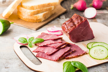 Fresh sliced marbled beef pastrami and vegetables on a cutting board. American delicacy. Rustic style