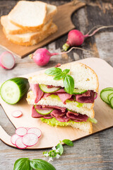 Double sandwich with pastrami and fresh vegetables and herbs on a cutting board. American snack. Rustic style. Vertical view