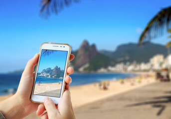 Girl in Ipanema Beach taking a photo with her mobile phone. Photographing with a camera of a smartphone in Rio de Janeiro, Brazil.