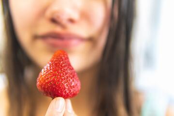 selective focus of a strawberry in the foreground being held between her fingers by a woman with an unfocused face