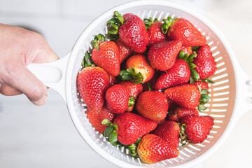 Hand holding a bowl with red strawberries