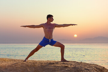 Fototapeta na wymiar Young man practicing yoga at the seashore