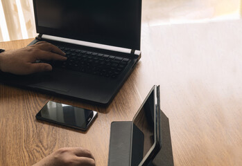 Man using laptop in office while using tablet and smartphone to make video calls