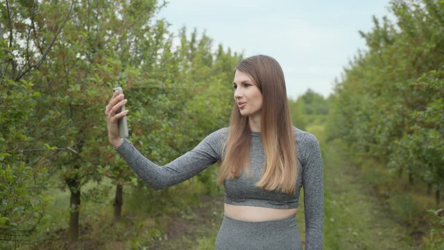 A modern sports woman takes pictures on the nature smartphone, recording a video blog. Sports video vlog. Video Blog athlete. Girl blogger points to the camera nature
